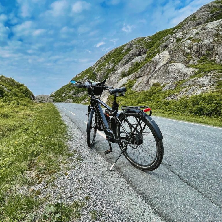 Schwarzes Fahrrad auf einer ruhigen Straße zwischen grünen Wiesen und Bergen.